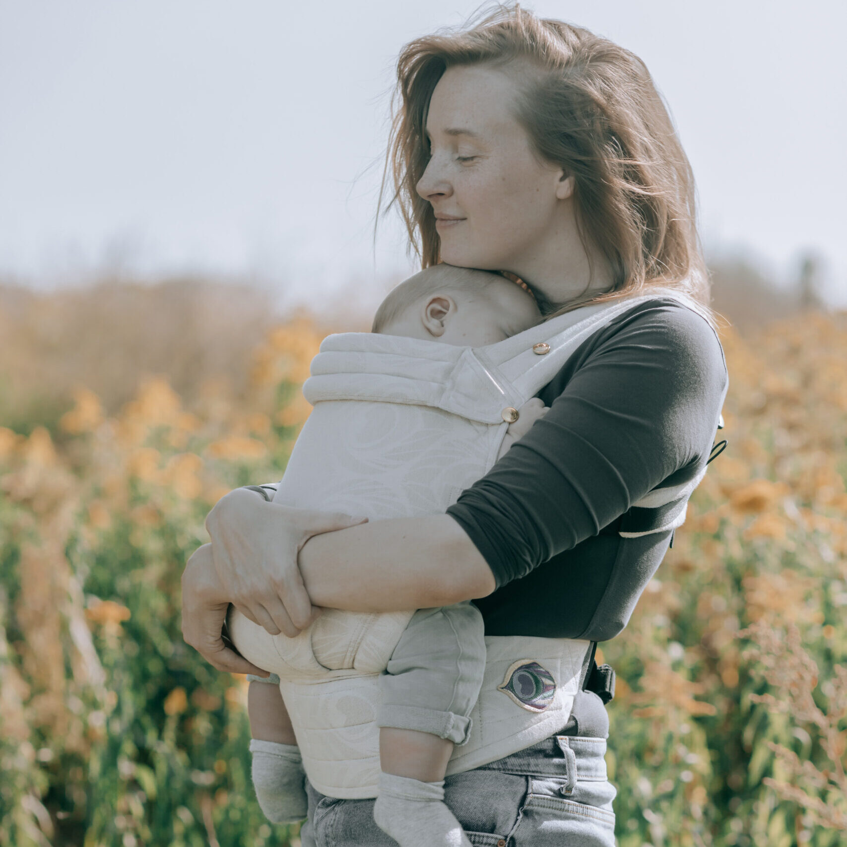 Baby slapend in de draagzak buiten, geknuffeld door mama – een liefdevolle manier om je kindje te ondersteunen zonder gecontroleerd laten huilen